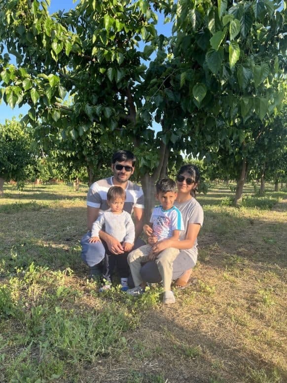 Una pareja se arrodilla junto a dos niños pequeños bajo un árbol de moras entre las hileras del huerto