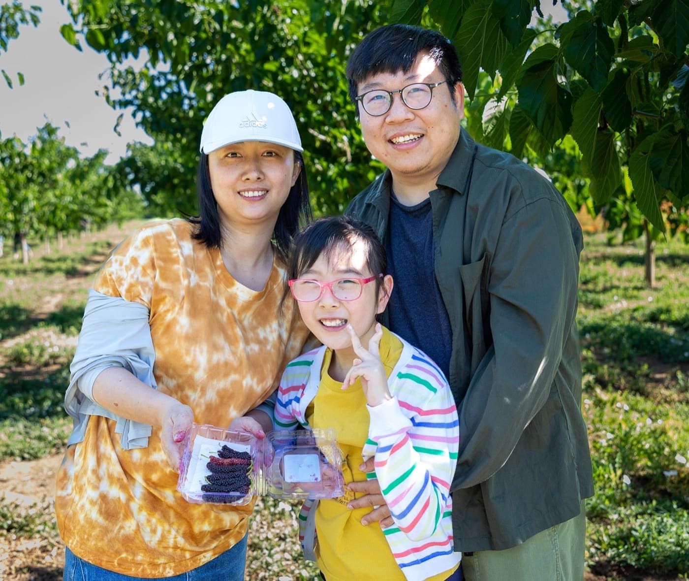 Una mamá, un papá y una hija con lentes rosados sostienen dos envases de moras frescas