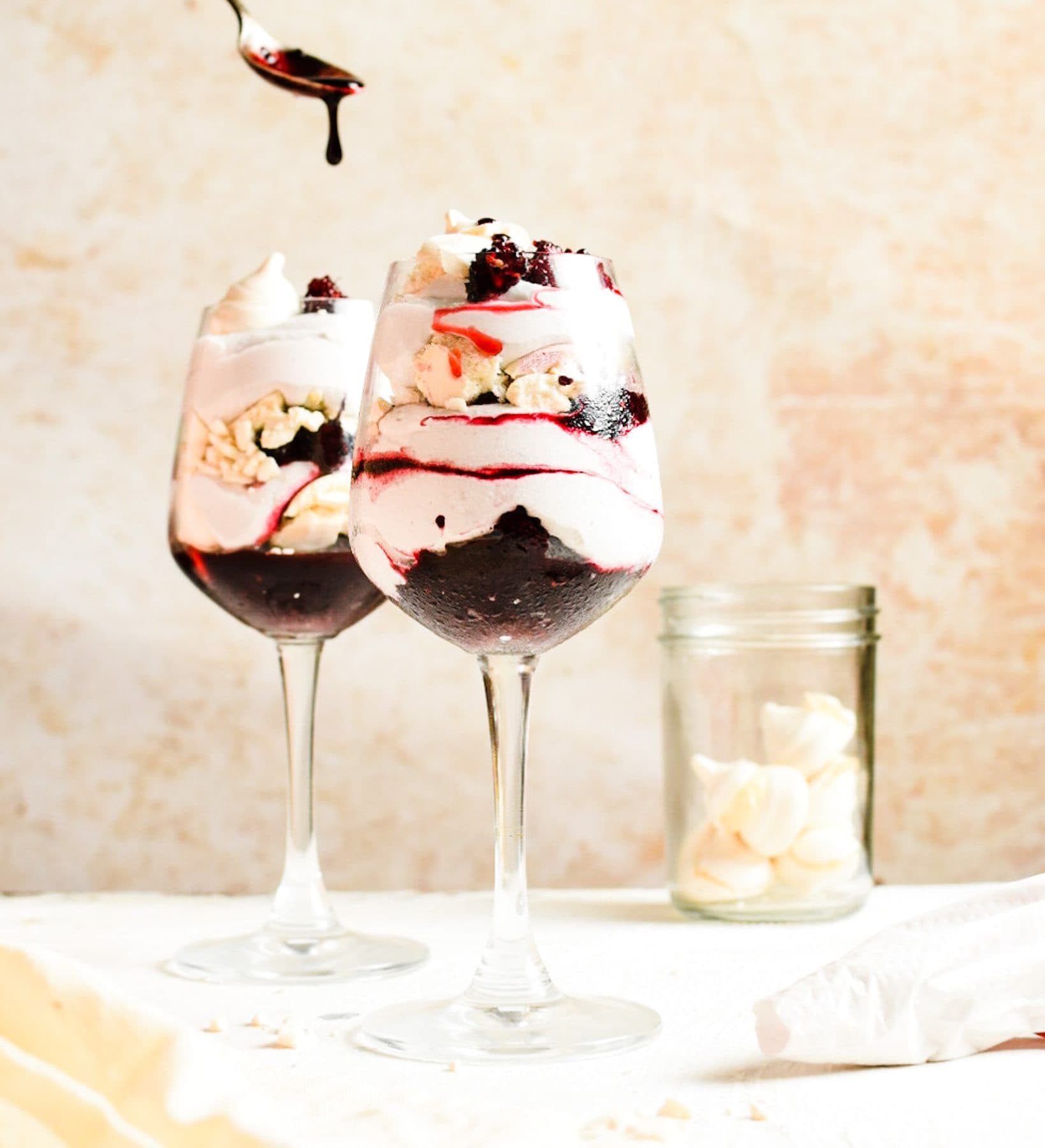 Dos copas de Eton mess de mora en capas de crema batida, merengue y compota, con una cuchara vertiendo más compota encima, Brentwood, CA