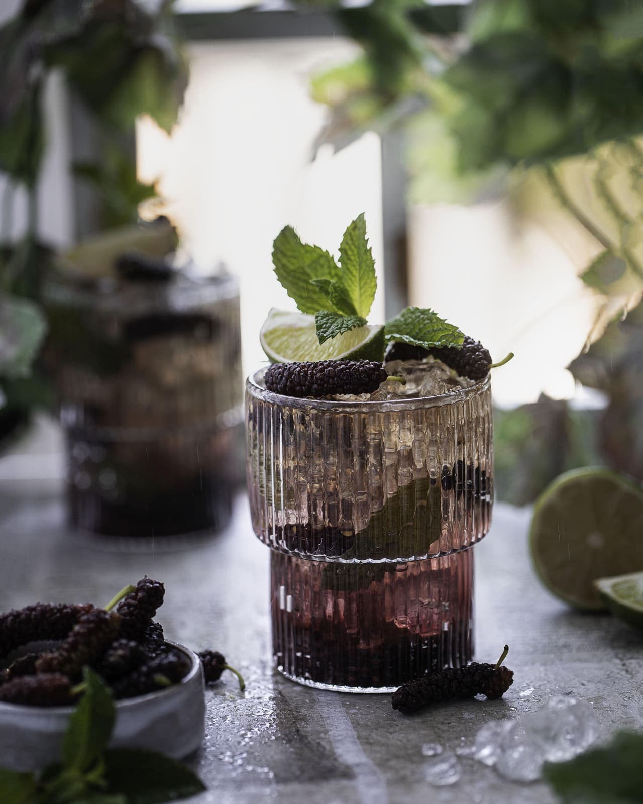 Vaso acanalado de mojito de mora con hielo, ramitas de menta, una rodaja de lima y moras frescas, sobre una mesa salpicada de lluvia, Brentwood, CA