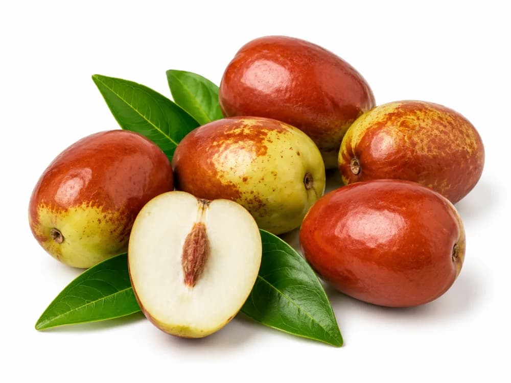 Fresh red-and-green jujubes with green leaves and one fruit cut open to show its pit, on a white background