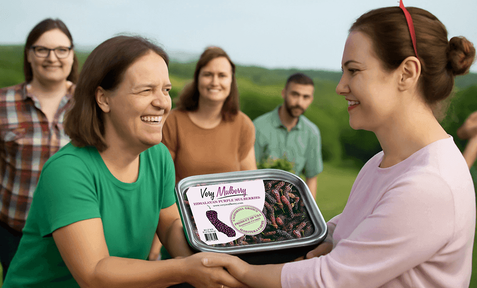 Dos mujeres estrechándose la mano mientras intercambian una bandeja de moras del Himalaya de Very Mulberry en un evento de recaudación de fondos